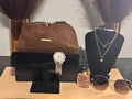 Collection of luxury items including a brown handbag, watch, sunglasses, and perfume on a table.