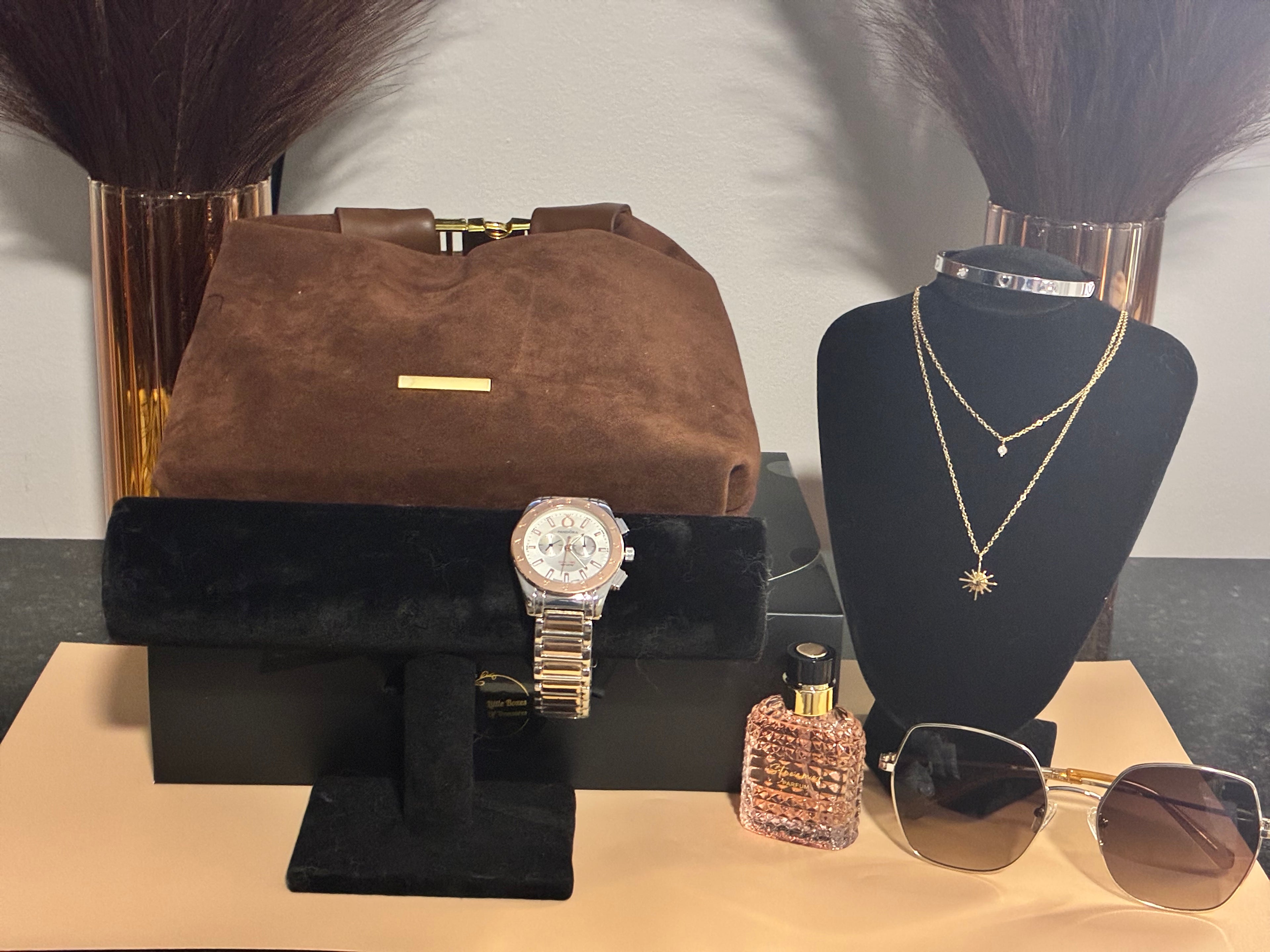 Collection of luxury items including a brown handbag, watch, sunglasses, and perfume on a table.