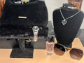 Jewelry display with a black velvet box, silver watch, perfume bottle, and sunglasses on a wooden surface.