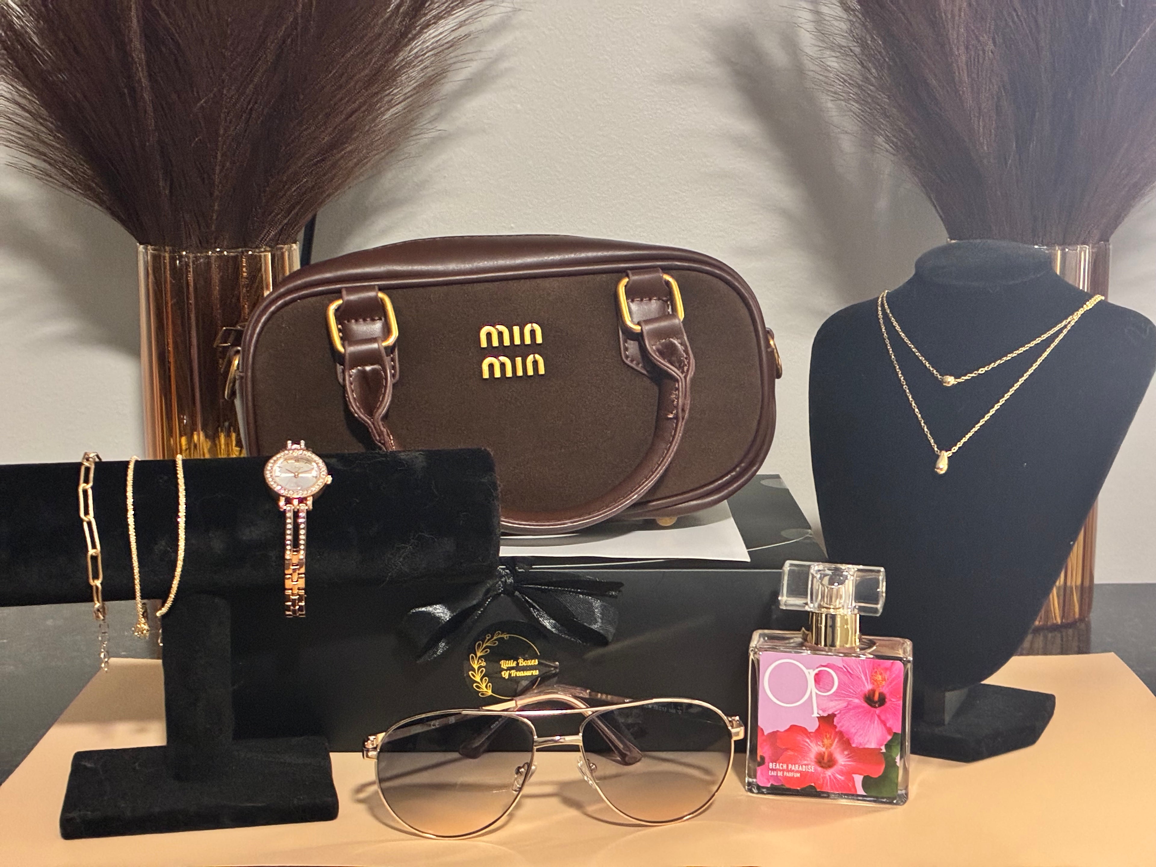 Collection of fashion items including a handbag, sunglasses, perfume, and jewelry on a table.
