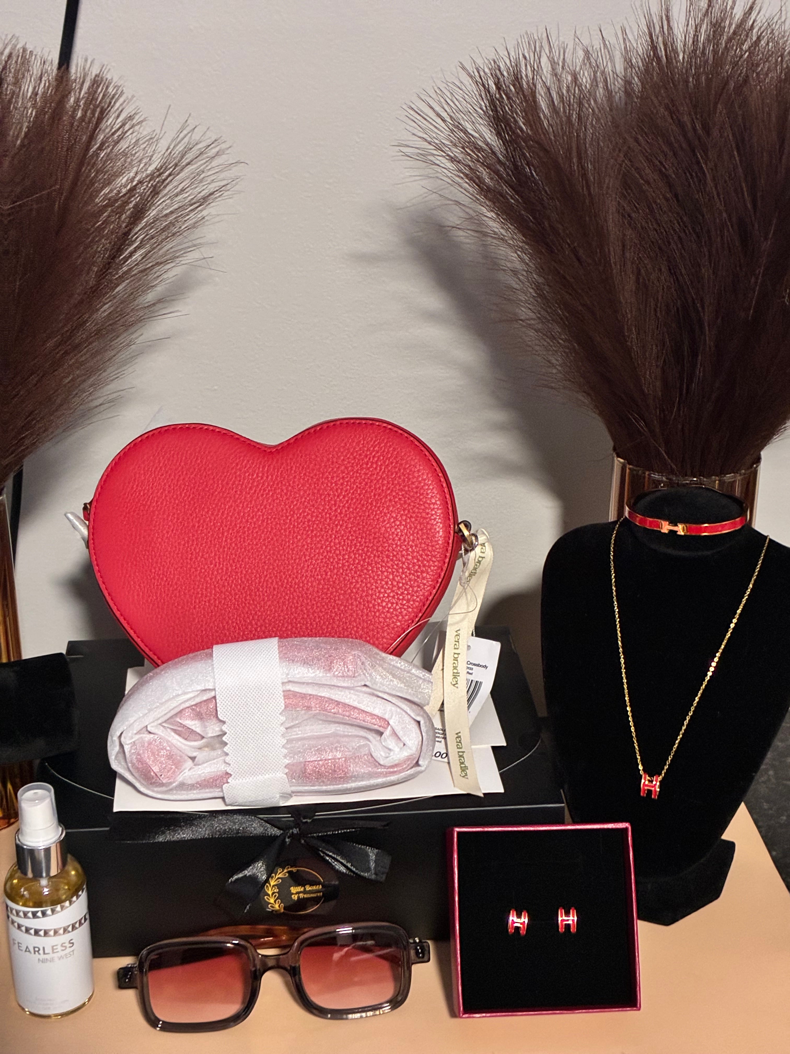 Collection of beauty products including a red pouch, sunglasses, and a bottle on a neutral background.