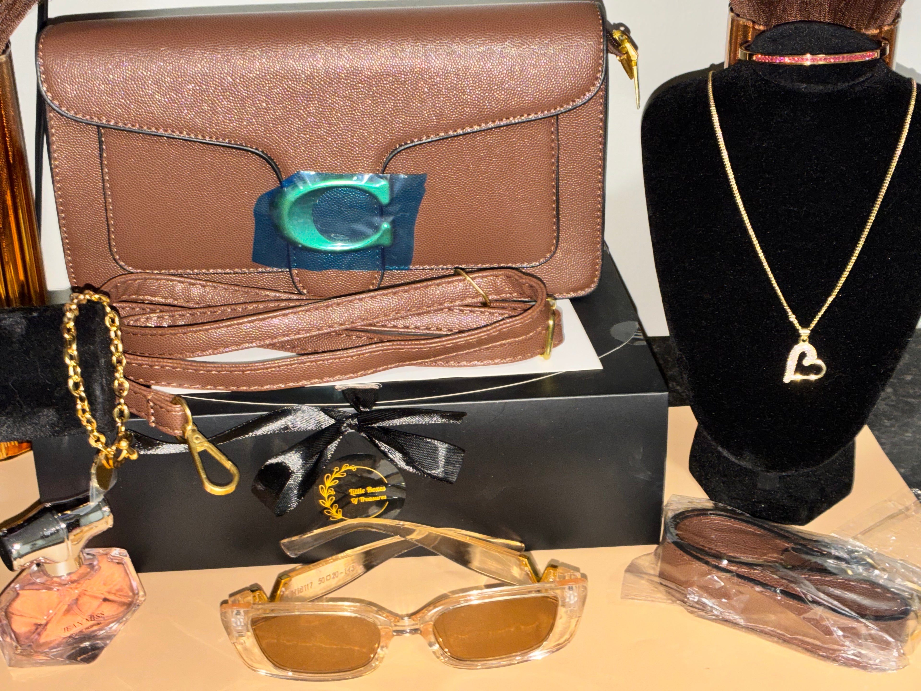 Brown handbag, sunglasses, perfume bottle, and necklace on a table.